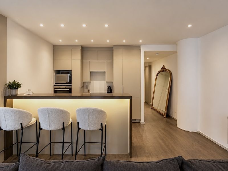 Modern open-plan kitchen featuring sleek built-in cabinetry, integrated appliances, and a stylish breakfast bar with ambient under-counter lighting.