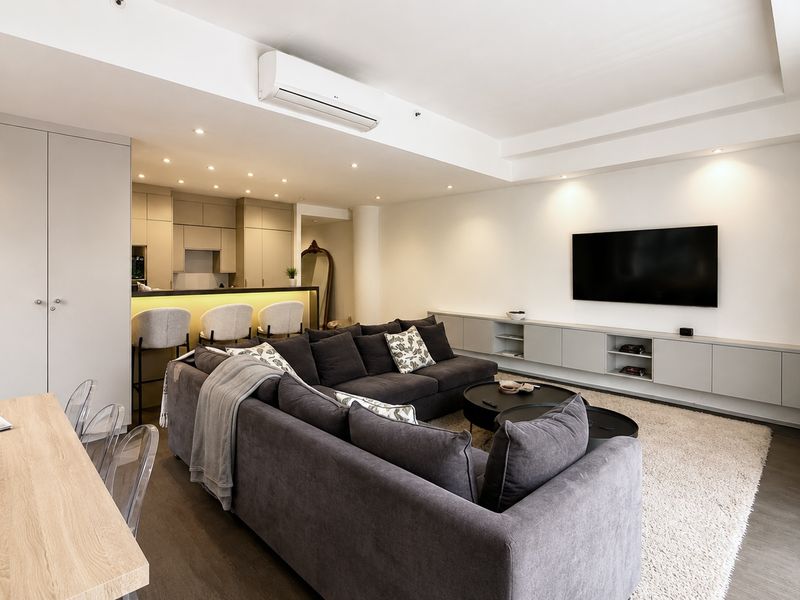 Modern open-plan living area featuring a sleek kitchen with island, built-in cabinetry, recessed lighting, and split-system air conditioning in a well-maintained apartment.