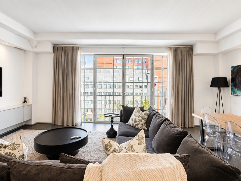Modern open-plan living and dining area featuring sleek built-in cabinetry, recessed lighting, polished concrete floors, and large windows with urban views.