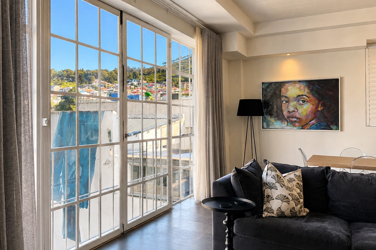 A bright living room featuring large glass french doors that provide natural light and views, complemented by recessed ceiling lighting and dark timber flooring.