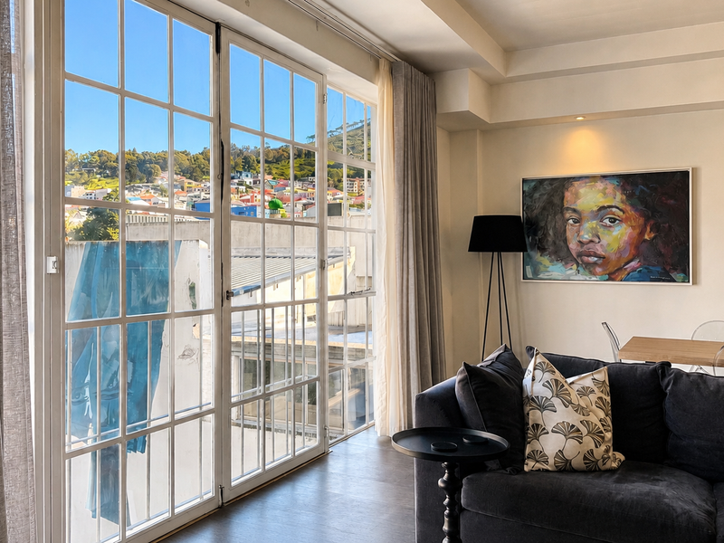 A bright living room featuring large glass french doors that provide natural light and views, complemented by recessed ceiling lighting and dark timber flooring.