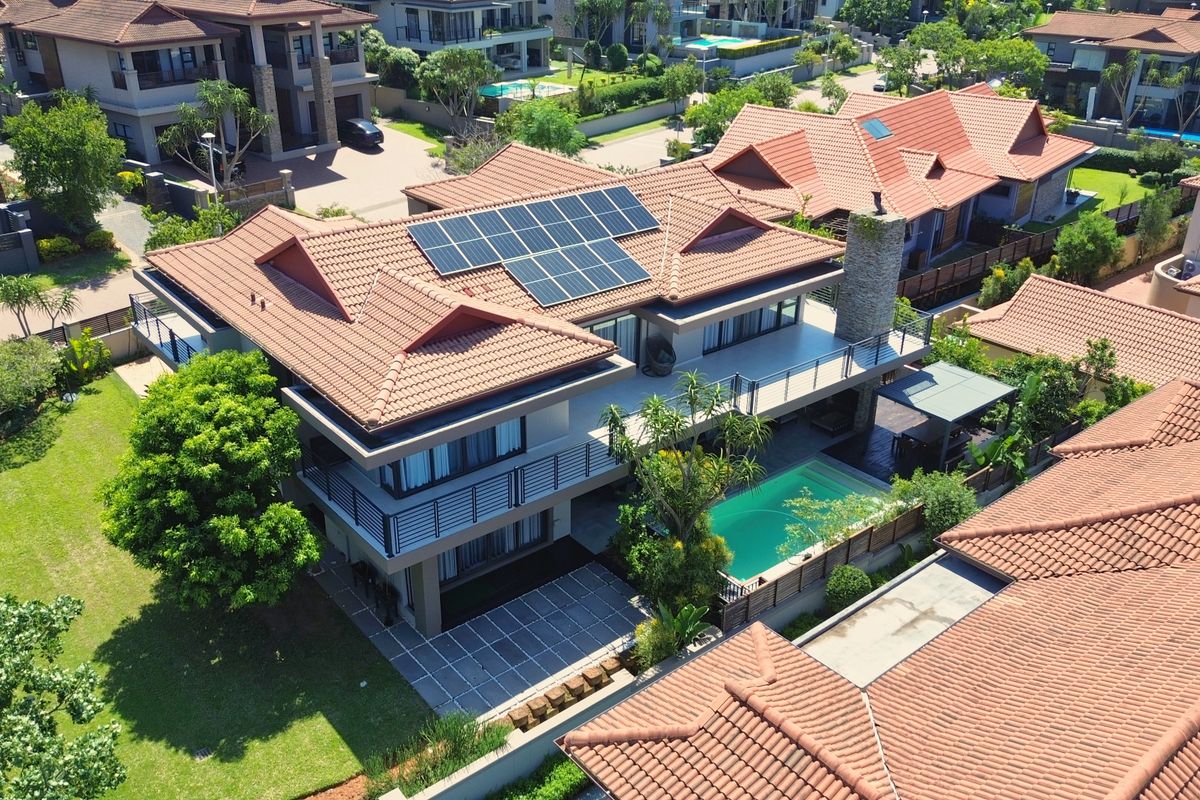 Aerial view of a modern residential property featuring a tiled roof with solar panels, a swimming pool, and a spacious balcony.