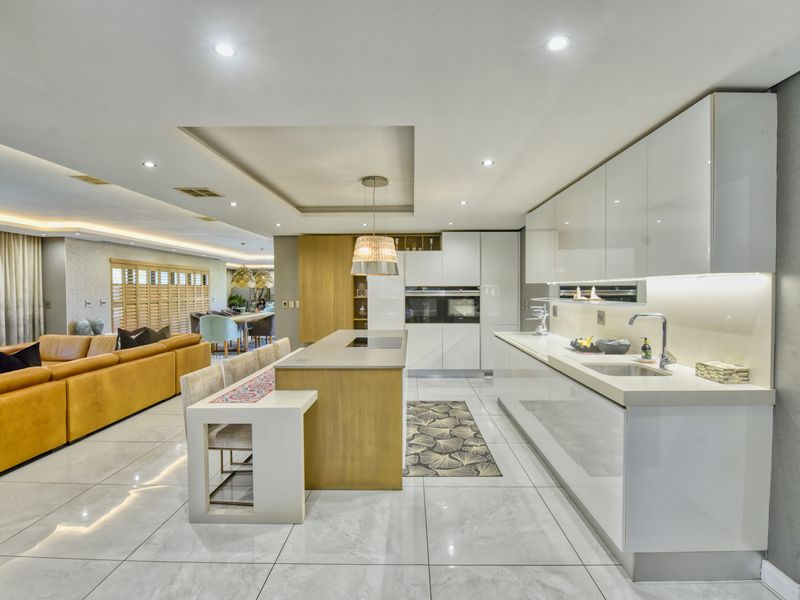 Modern open-plan kitchen featuring high-gloss cabinetry, stone countertops, a central island with integrated hob, and sleek porcelain flooring, seamlessly flowing into the living area.