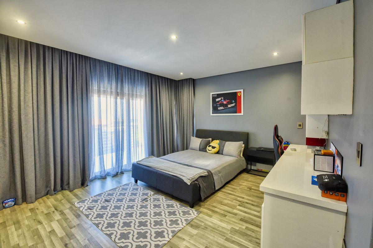 A well-maintained bedroom featuring laminate flooring, recessed downlighting, a built-in desk, and large sliding glass doors with floor-to-ceiling curtains.