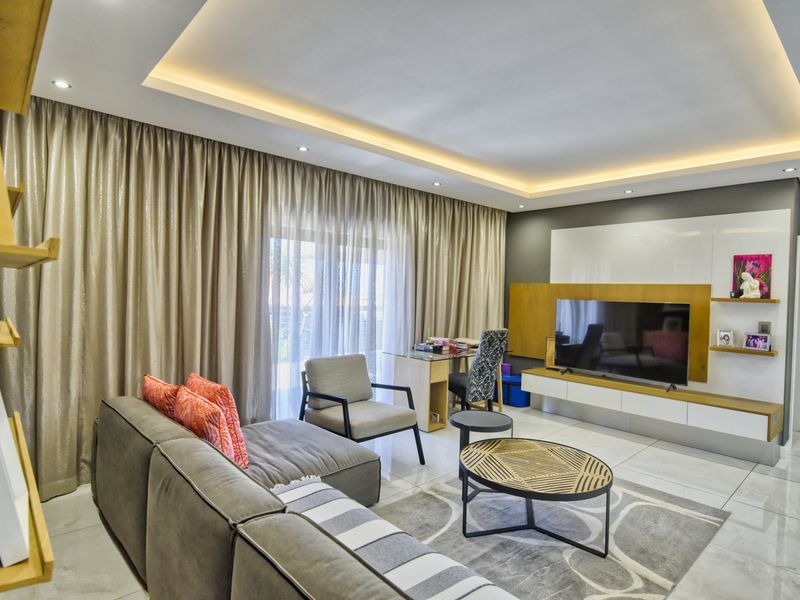 Modern living room featuring tiled flooring, recessed cove lighting, and a sleek built-in media console with integrated shelving.