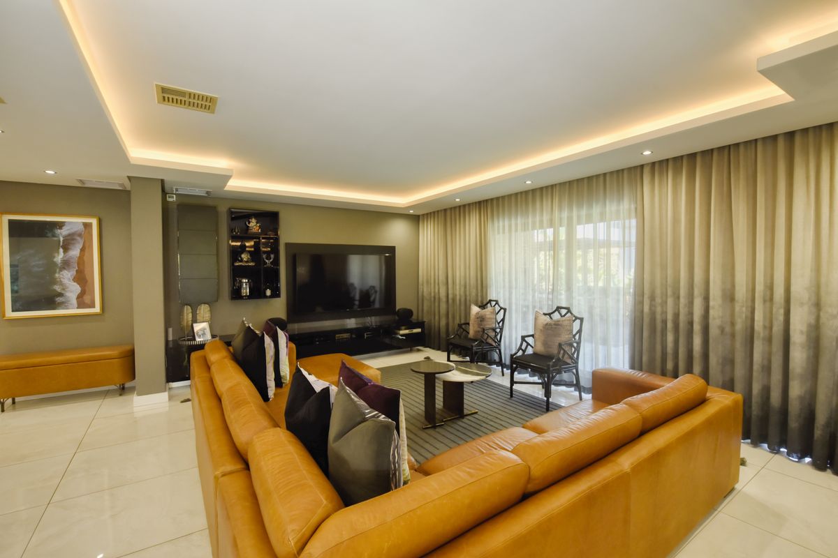 Spacious living room featuring modern recessed cove lighting, sleek tiled flooring, and large sliding glass doors leading to an outdoor area.