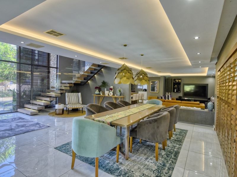 Spacious open-plan living and dining area featuring a modern floating staircase, high-end porcelain tiling, and extensive floor-to-ceiling windows with recessed ambient lighting.