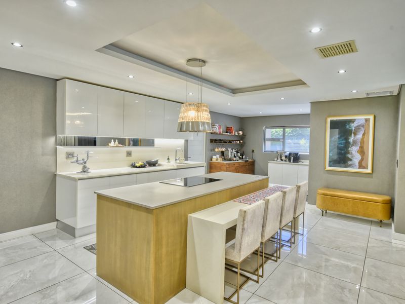 Modern kitchen featuring a large central island with integrated cooktop, sleek high-gloss cabinetry, stone countertops, and elegant recessed lighting throughout.