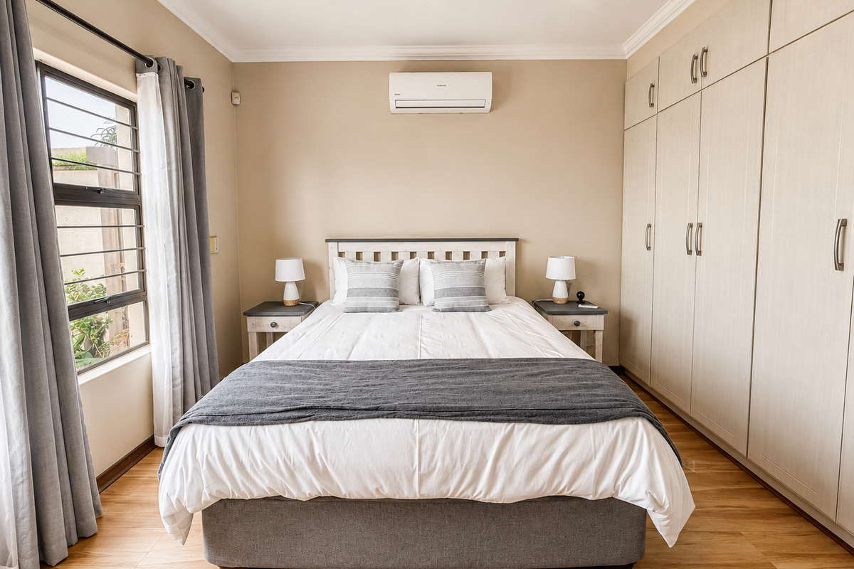 A well-maintained bedroom featuring light-toned laminate flooring, extensive built-in cabinetry, and a wall-mounted air conditioning unit.