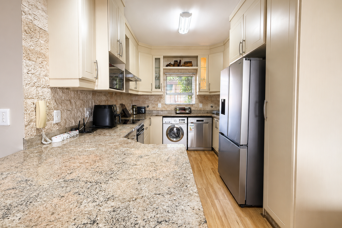 A well-appointed galley kitchen featuring granite countertops, stone tile backsplash, integrated appliances, and ample built-in cabinetry with light wood-look flooring.