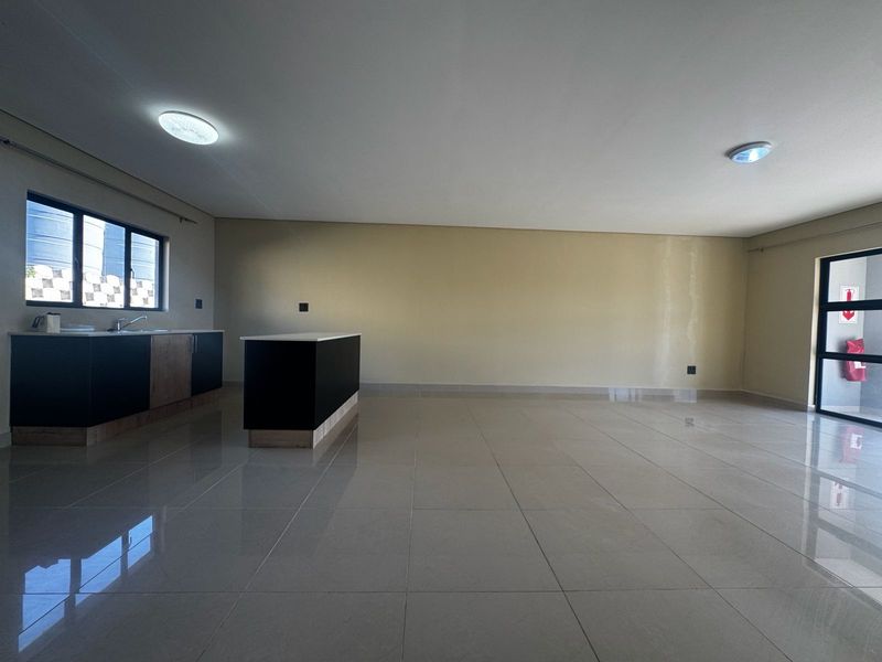 Spacious open-plan living area featuring tiled flooring, a modern kitchen island, and neutral wall finishes, offering a versatile layout for dining and relaxation.