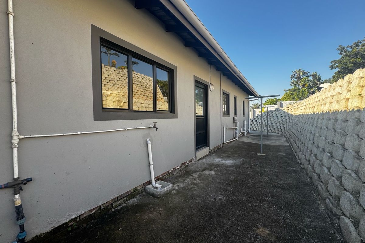 Rear exterior view of the apartment featuring a concrete pathway, retaining wall, and external plumbing fixtures.