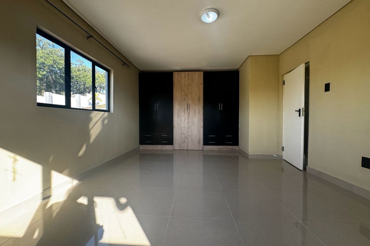 A bright, empty bedroom featuring modern built-in cupboards with a two-tone finish, neutral tiled flooring, and large windows allowing for ample natural light.