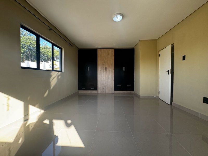 A bright, empty bedroom featuring modern built-in cupboards with a two-tone finish, neutral tiled flooring, and large windows allowing for ample natural light.