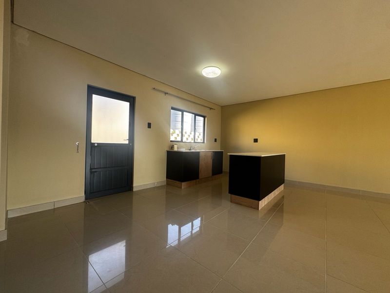 An open-plan living and kitchen area featuring modern cabinetry, a central island, tiled flooring, and direct access to an exterior door.