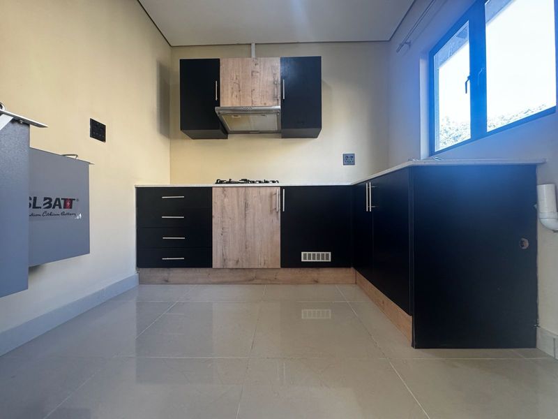 Modern kitchen featuring sleek black and wood-grain cabinetry, stone countertops, a gas hob with extractor fan, and polished tiled flooring.