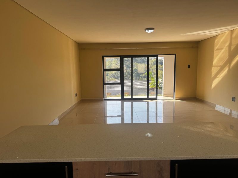 Spacious open-plan living area featuring modern quartz countertops, large sliding glass doors leading to an outdoor space, and polished porcelain floor tiles.