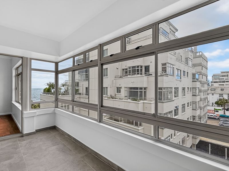 An enclosed balcony featuring large aluminium-framed windows, tiled flooring, and views of the surrounding urban landscape and ocean.