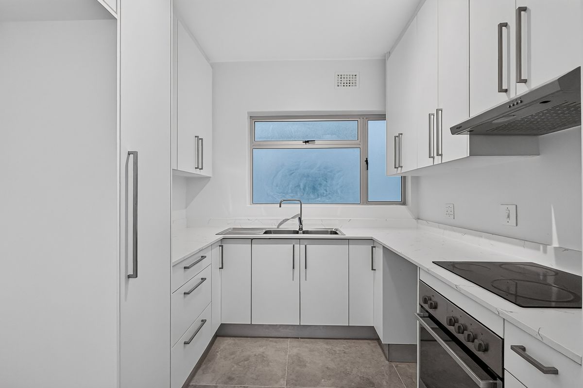 A modern, clean-lined kitchen featuring white cabinetry, stone countertops, integrated appliances, and neutral tiled flooring, offering a bright and functional workspace.