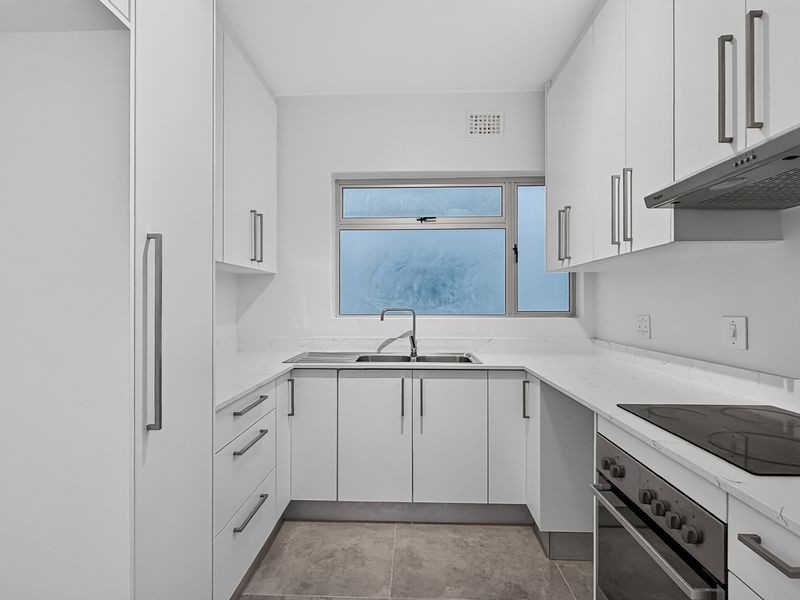 A modern, clean-lined kitchen featuring white cabinetry, stone countertops, integrated appliances, and neutral tiled flooring, offering a bright and functional workspace.