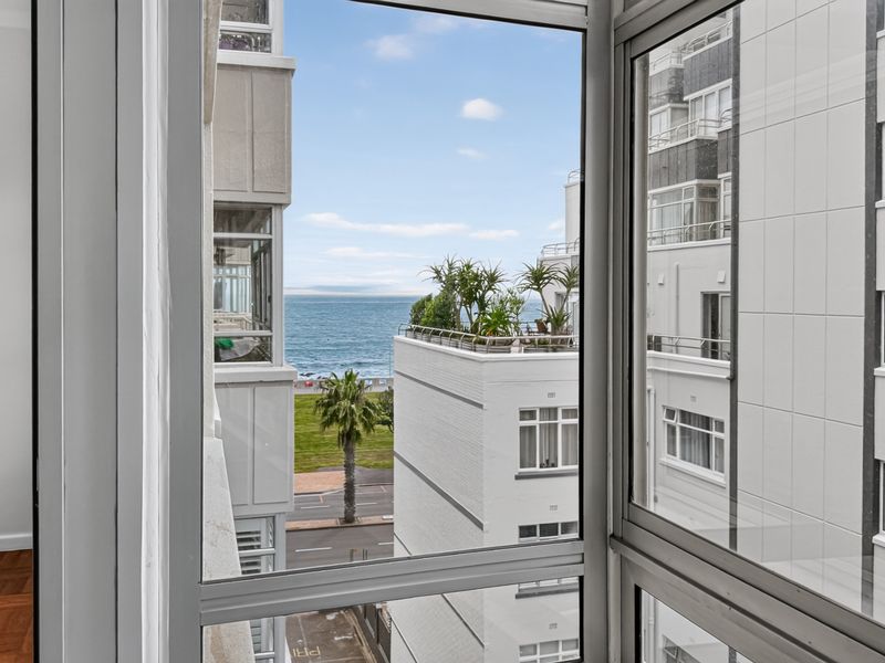 A view from an apartment window overlooking the street, neighbouring buildings, and the ocean.