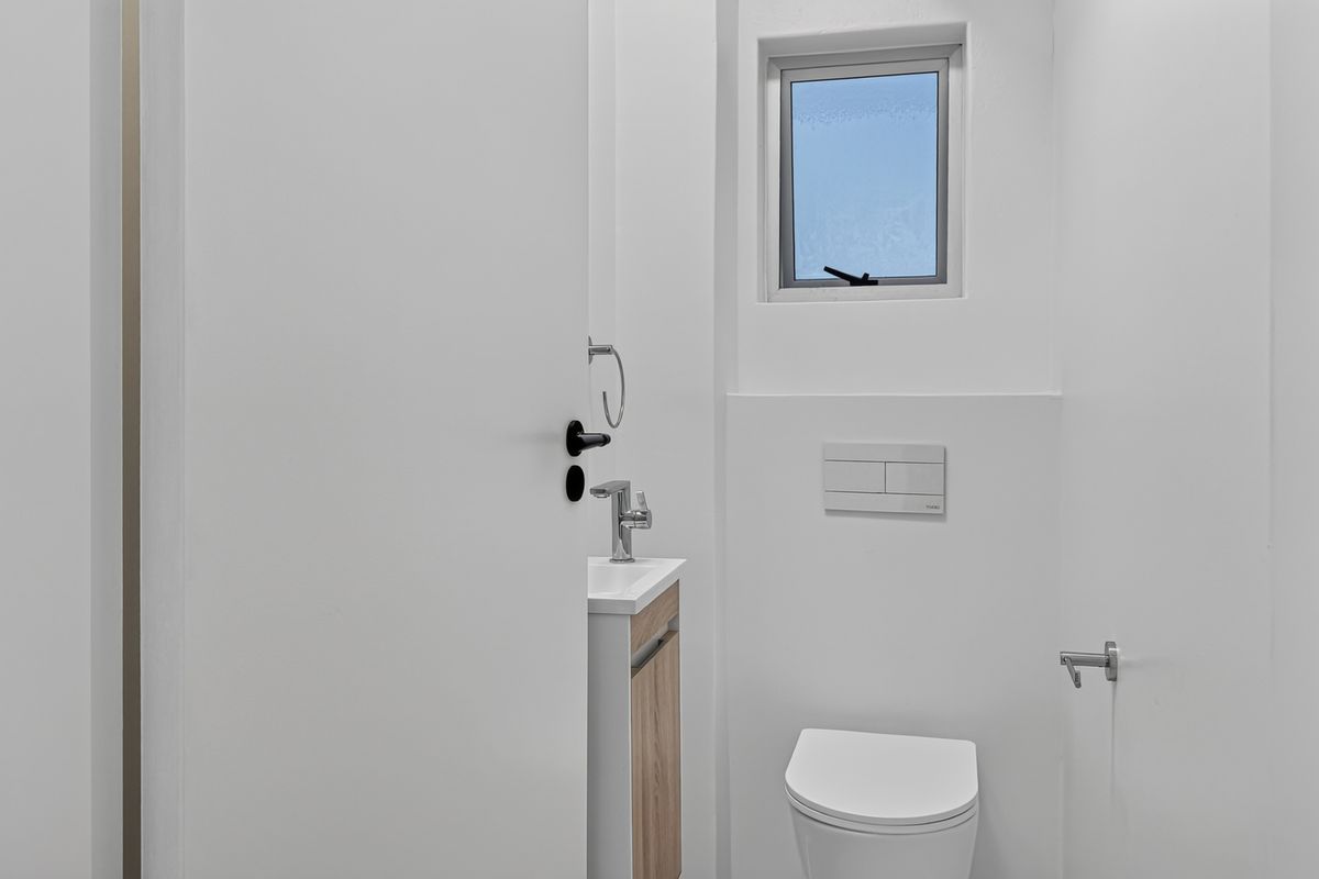 A modern, minimalist guest bathroom featuring a wall-hung toilet with a concealed cistern, a compact vanity cabinet, and a small casement window.