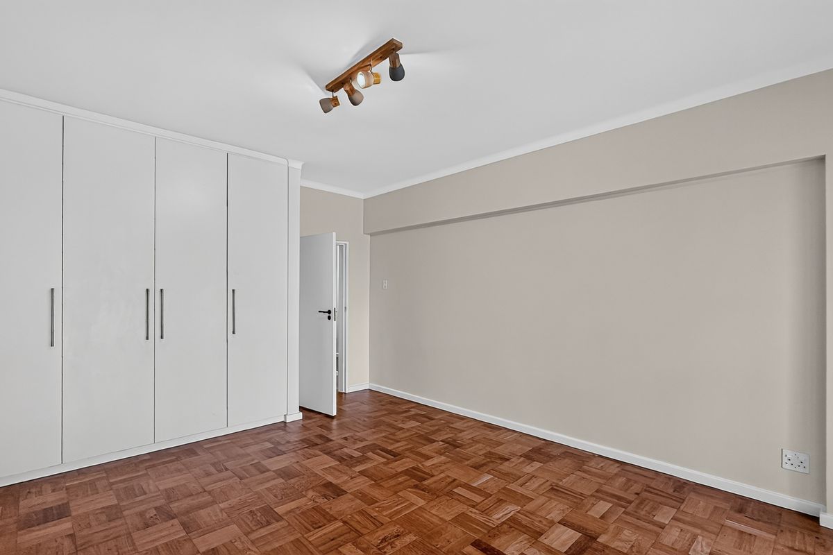 A bright, empty bedroom featuring classic parquet flooring and extensive built-in cupboard storage, providing a clean and versatile space.