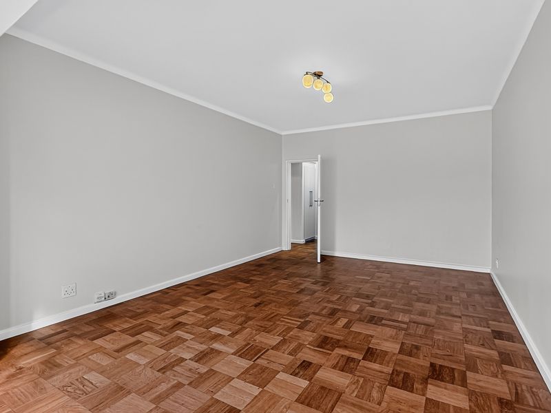 A bright, empty living room featuring well-maintained parquet flooring and neutral wall finishes.