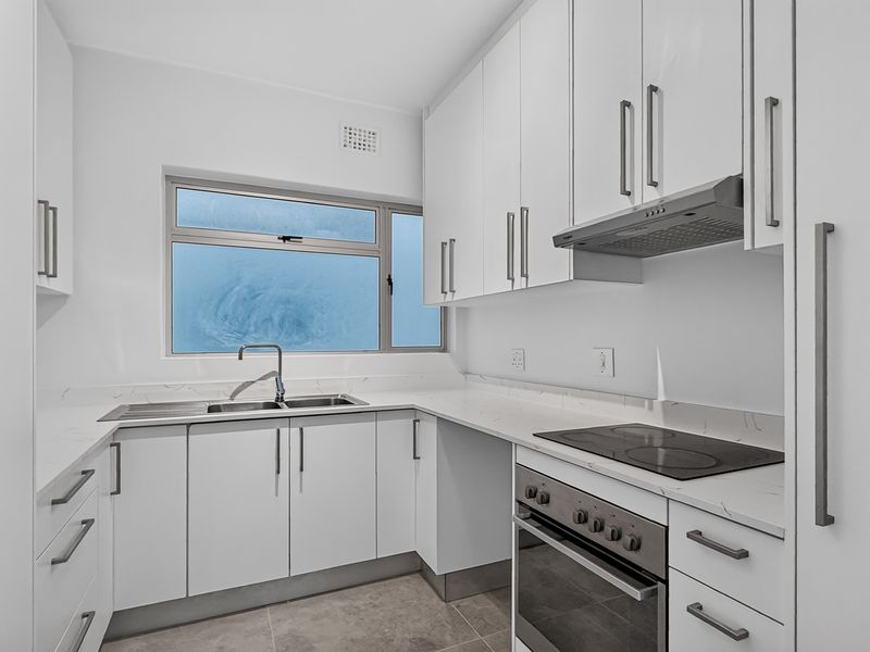 A modern, clean kitchen featuring white cabinetry, stone countertops, integrated stainless steel appliances, and a functional layout with ample storage space.