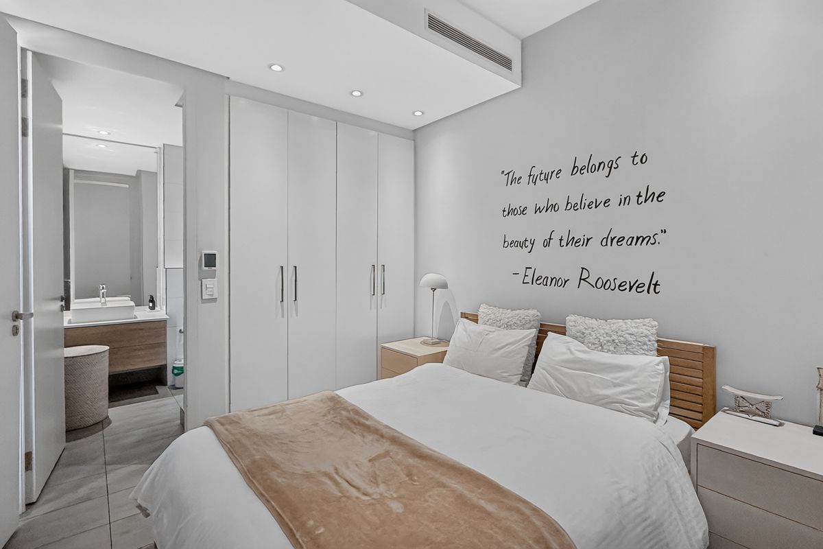 Modern bedroom featuring built-in cupboards, recessed lighting, ducted air conditioning, and an adjoining en-suite bathroom with contemporary finishes.