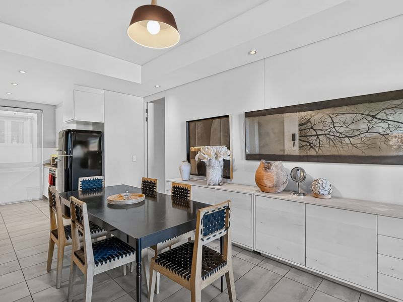 A bright open-plan living and dining area featuring modern tiled flooring, recessed lighting, and sleek built-in cabinetry.