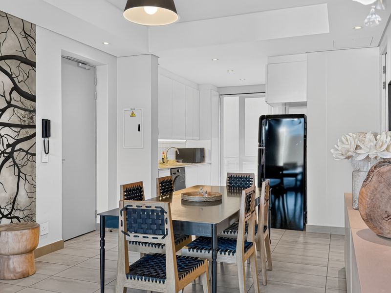 Modern open-plan living and dining area featuring neutral tiled flooring, recessed lighting, and a sleek kitchen with built-in cabinetry.