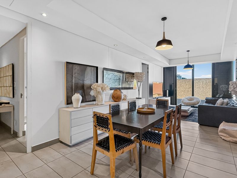 Spacious open-plan living and dining area featuring neutral tiled flooring, recessed lighting, and large sliding doors leading to an outdoor patio space.
