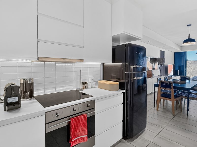 Modern open-plan kitchen featuring sleek white cabinetry, integrated appliances, and a subway tile backsplash, flowing seamlessly into the dining and living area.