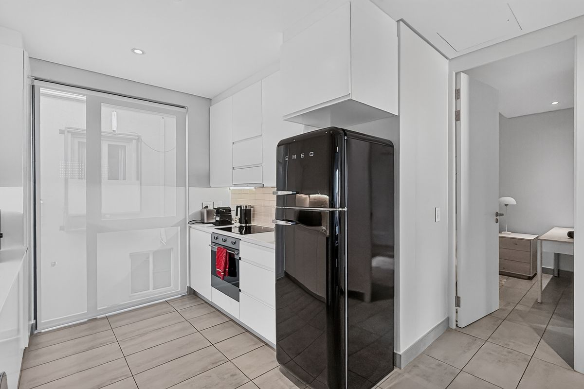 Modern kitchen featuring sleek white cabinetry, integrated oven, cooktop, and tiled flooring, with a clean, minimalist aesthetic and direct access to adjacent rooms.