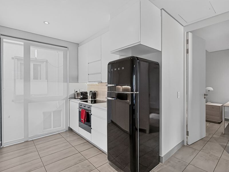 Modern kitchen featuring sleek white cabinetry, integrated oven, cooktop, and tiled flooring, with a clean, minimalist aesthetic and direct access to adjacent rooms.