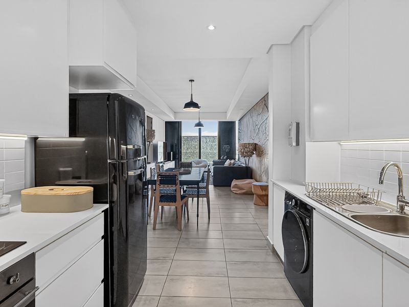 Modern open-plan kitchen and living area featuring sleek white cabinetry, integrated appliances, tiled flooring, and contemporary lighting, flowing seamlessly into the dining and lounge space.
