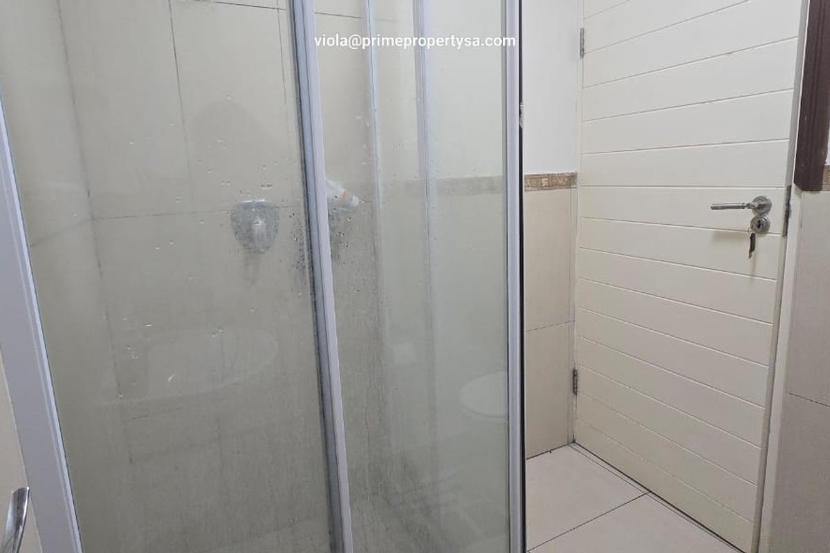 A functional bathroom featuring a glass shower enclosure and neutral wall and floor tiling.