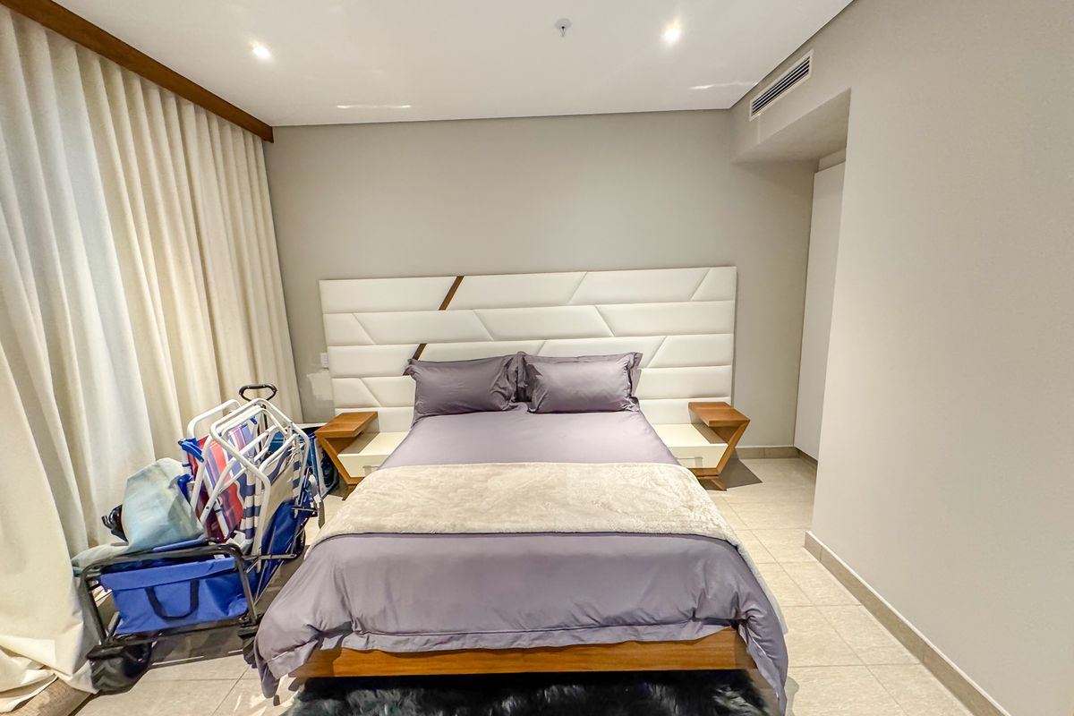 A well-maintained bedroom featuring tiled flooring, recessed lighting, and a modern built-in headboard with integrated bedside tables.