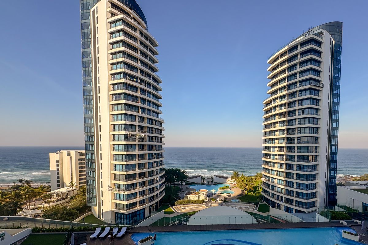 Aerial view of a modern high-rise apartment complex featuring swimming pools, landscaped grounds, and direct ocean views.