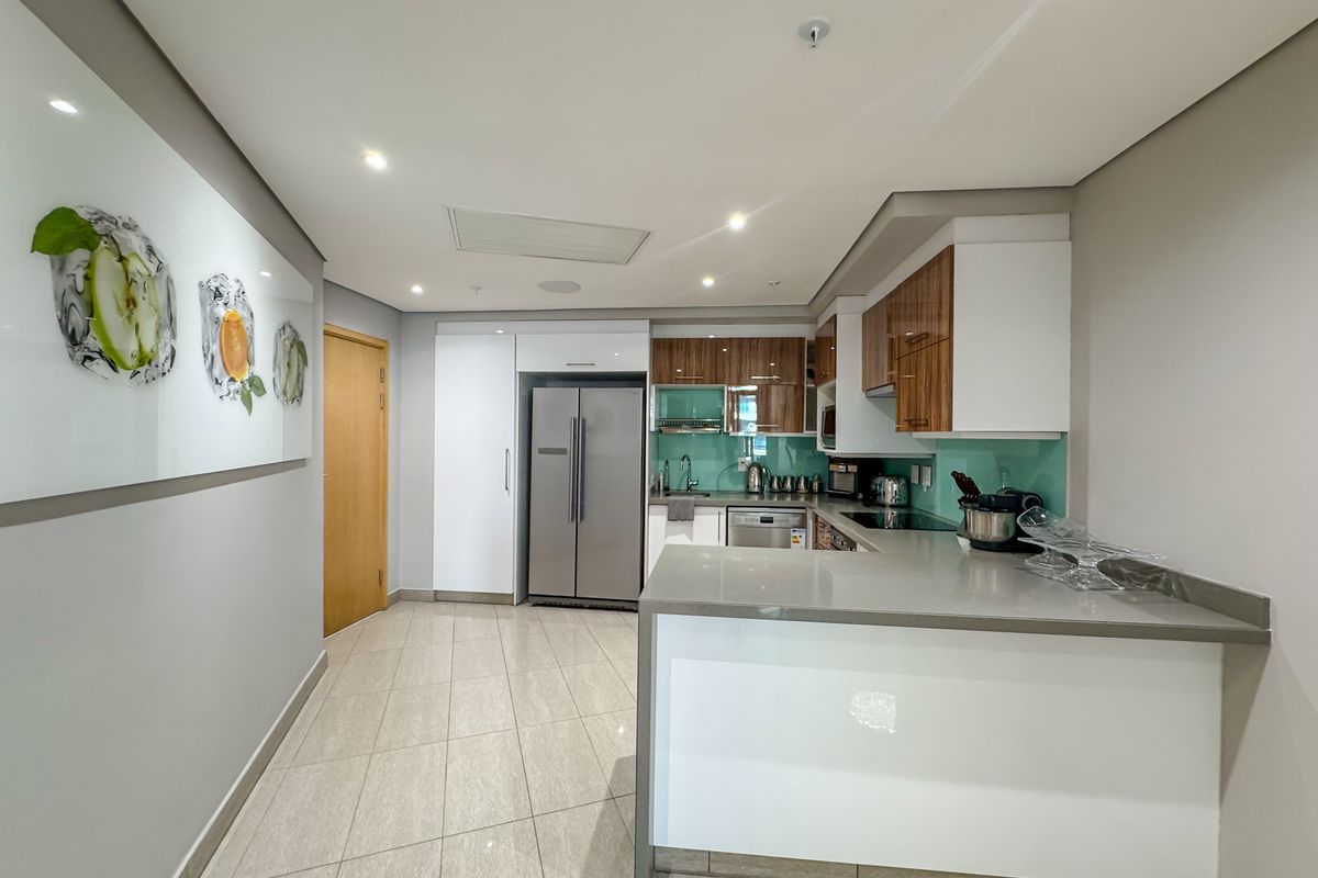 Modern kitchen featuring stone countertops, glass splashback, integrated appliances, and sleek cabinetry with recessed lighting and tiled flooring.