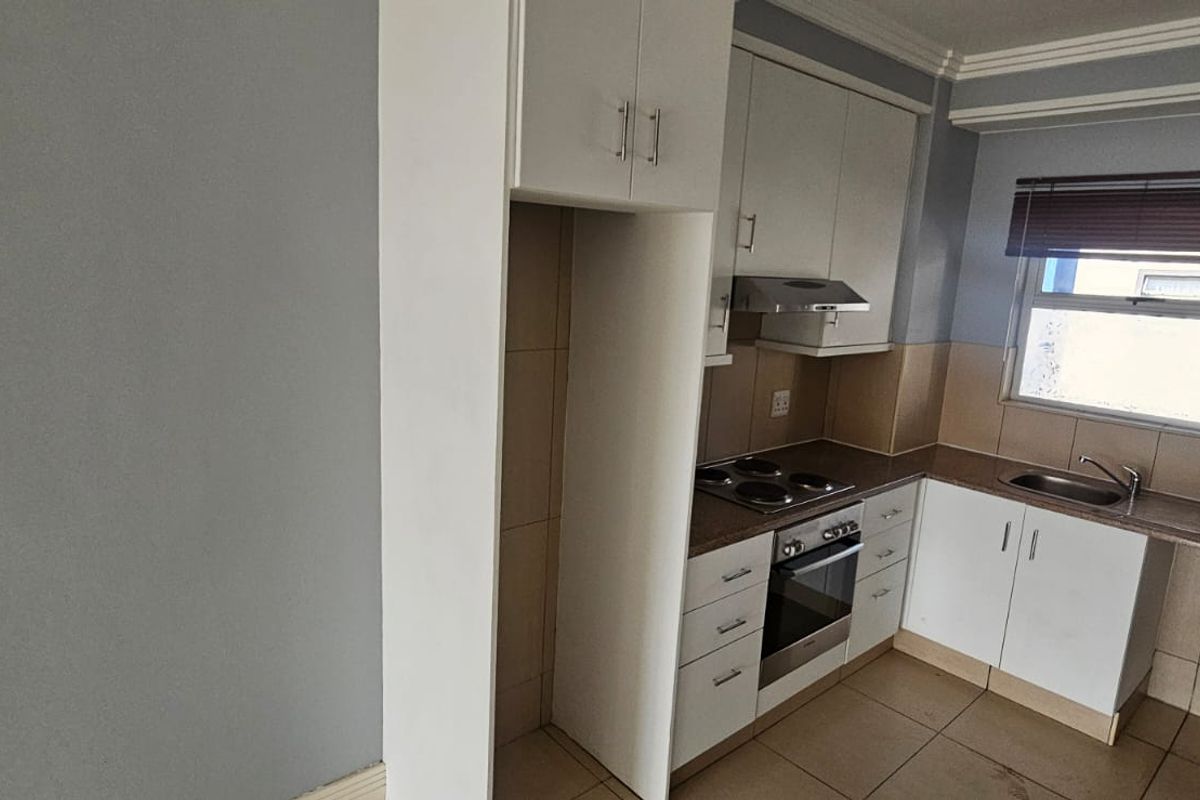 A clean, functional kitchen featuring white built-in cabinetry, an electric hob, oven, extractor fan, and tiled finishes throughout.