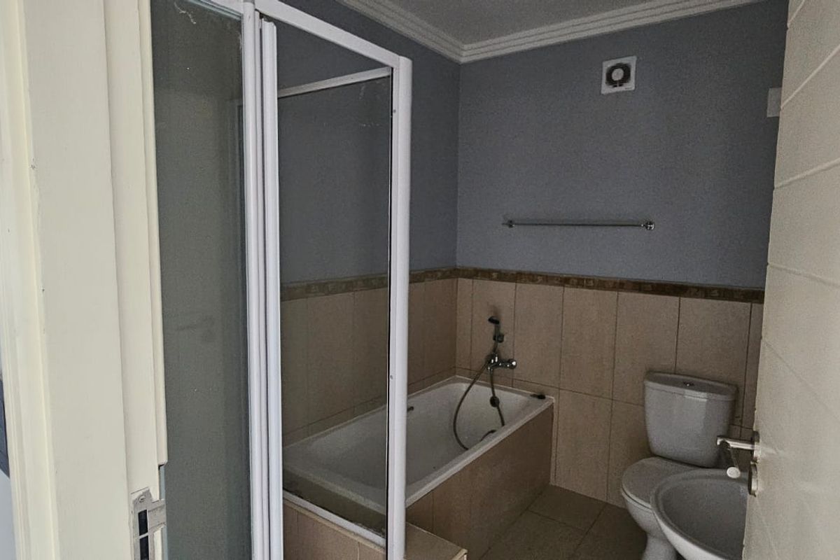 A functional bathroom featuring a built-in bathtub, separate shower enclosure, toilet, and washbasin with neutral wall tiling.