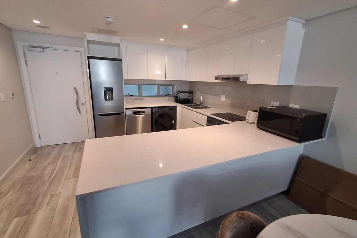 Modern kitchen featuring sleek white gloss cabinetry, quartz countertops, integrated appliances, and recessed lighting in an open-plan layout.