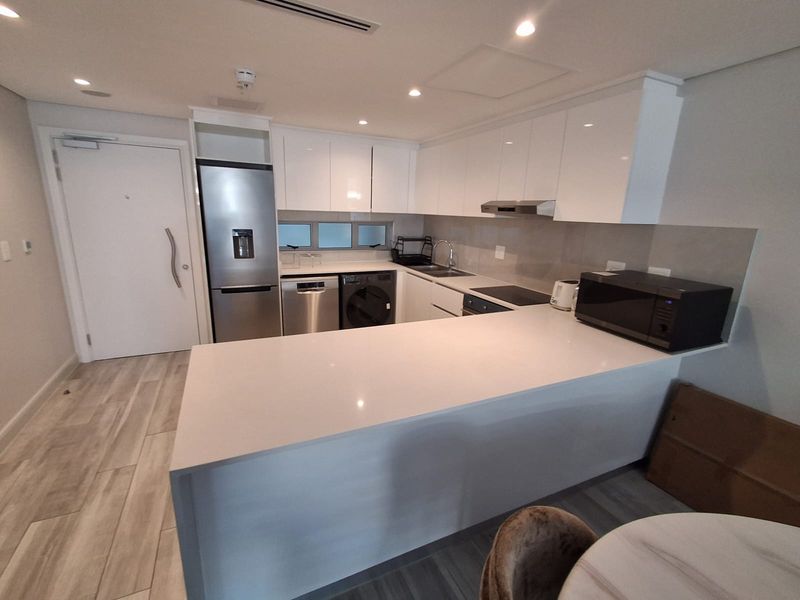 Modern kitchen featuring sleek white gloss cabinetry, quartz countertops, integrated appliances, and recessed lighting in an open-plan layout.