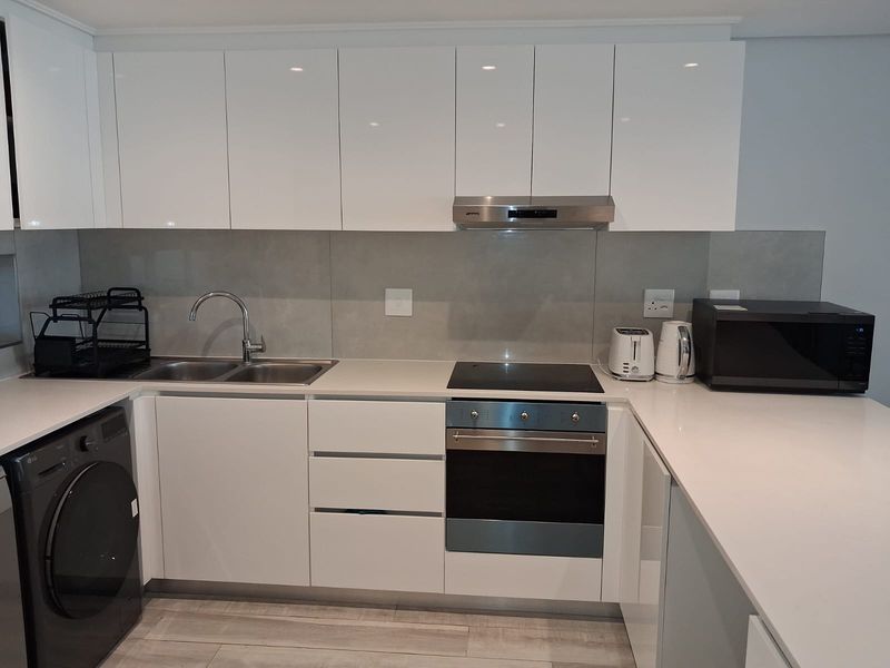 Modern kitchen featuring white gloss cabinetry, stone countertops, integrated appliances, and a sleek tiled splashback in a clean, contemporary layout.