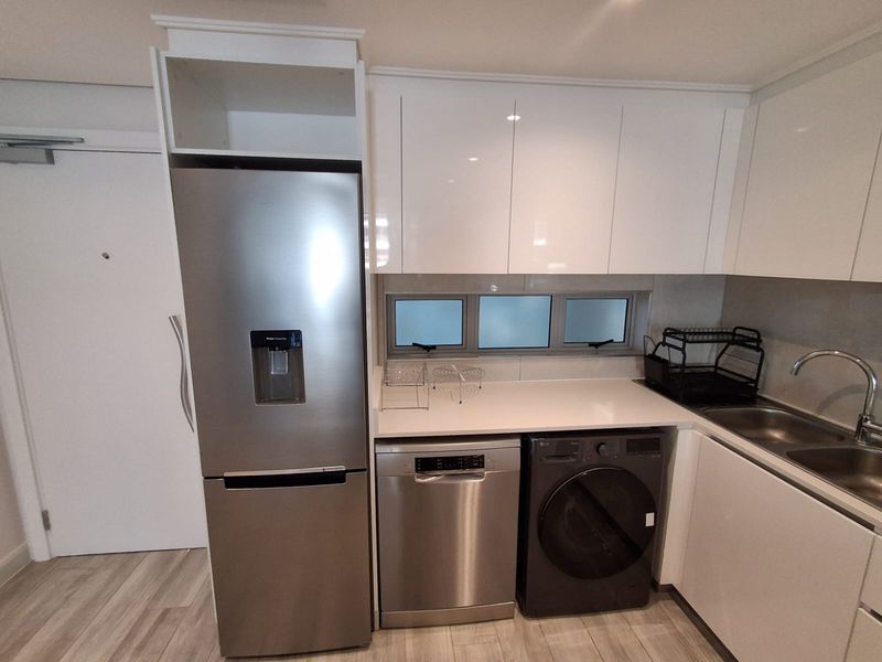 Modern kitchen featuring sleek white cabinetry, stone countertops, stainless steel sink, and integrated appliances, providing a clean and functional culinary space.