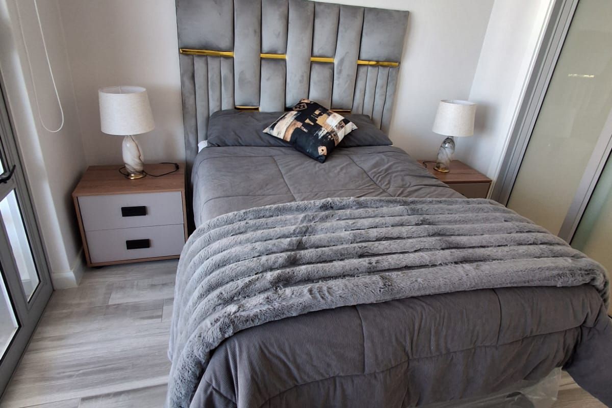 A modern bedroom featuring light-toned laminate flooring, a sliding glass door providing natural light, and a built-in wardrobe.