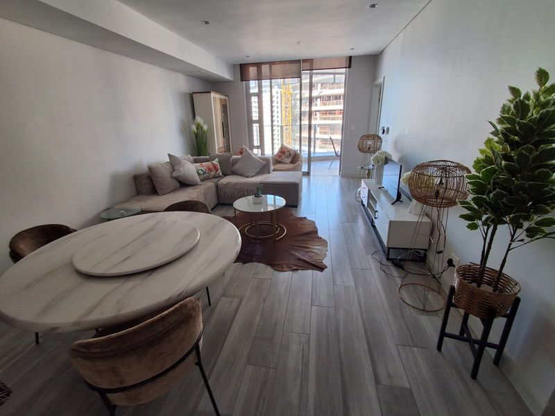 Modern open-plan living and dining area featuring wood-look tile flooring, recessed lighting, and large sliding glass doors leading to a balcony.