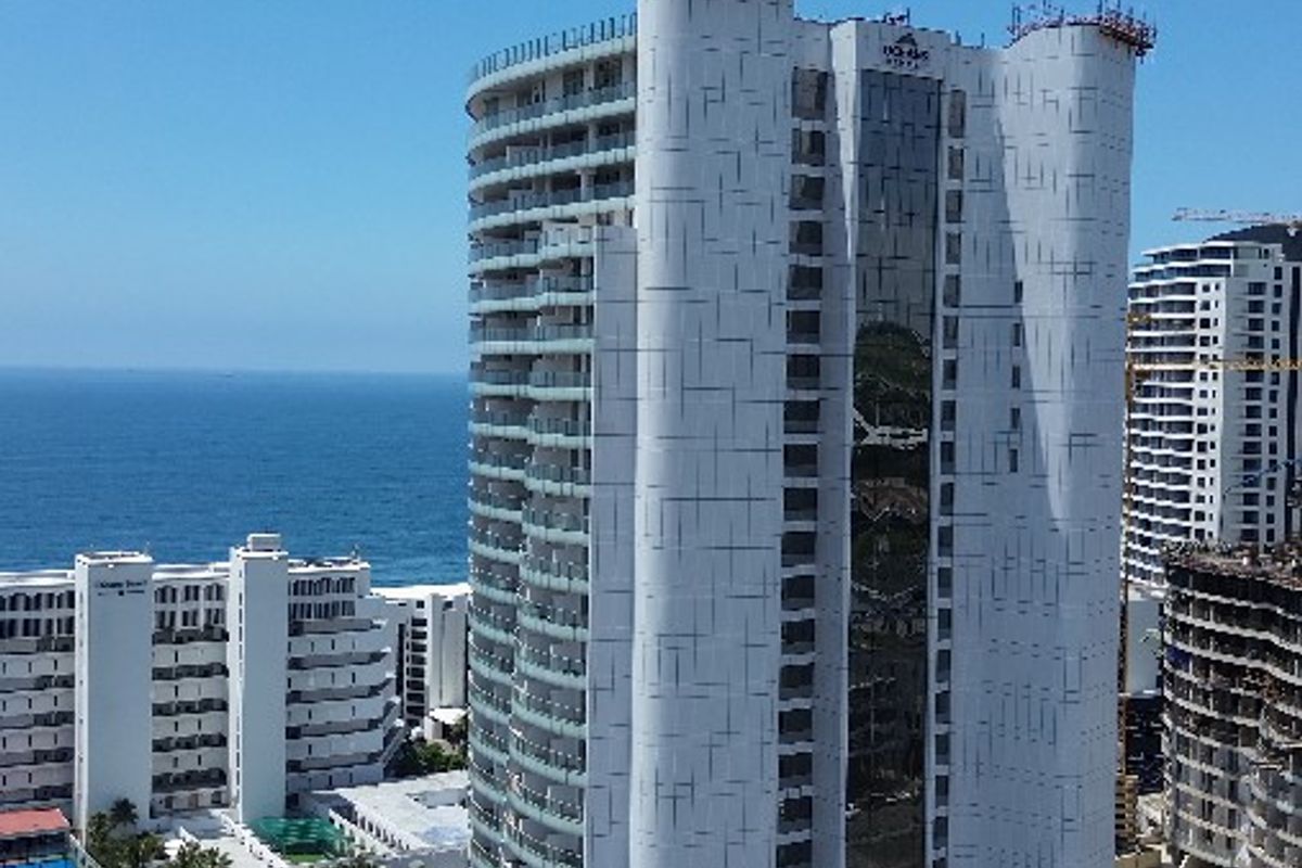 Aerial view of a modern high-rise apartment complex featuring balconies, a swimming pool, and landscaped grounds near the coastline.